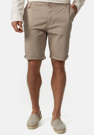 Beige shorts with rolled cuffs, made from lightweight fabric. Features front pockets and a button closure. Paired with light espadrilles.