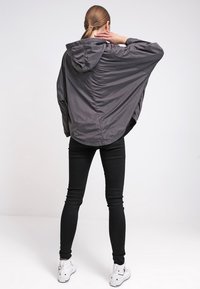 Mørkegrå hættetrøje med en loose, oversized fit og stramme manchetter, parret med sorte skinny jeans og hvide sneakers.
