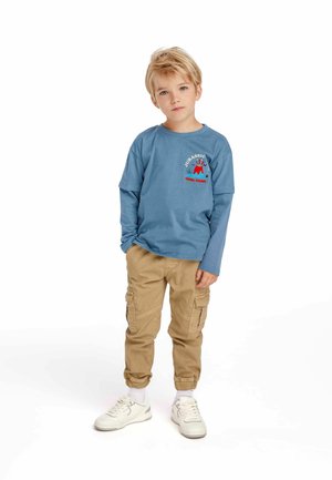 Blaues Langarm-T-Shirt mit Dinosaurier-Grafik und Text, kombiniert mit hellbeigen Cargo-Hosen und weißen Sneakers. Lässiger, entspannter Schnitt.