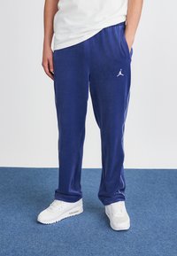 Tengerészkék melegítőnadrág fehér oldalsávokkal és Jumpman logóval, puha anyagból készült, rugalmas derékkal és oldalsó zsebekkel.