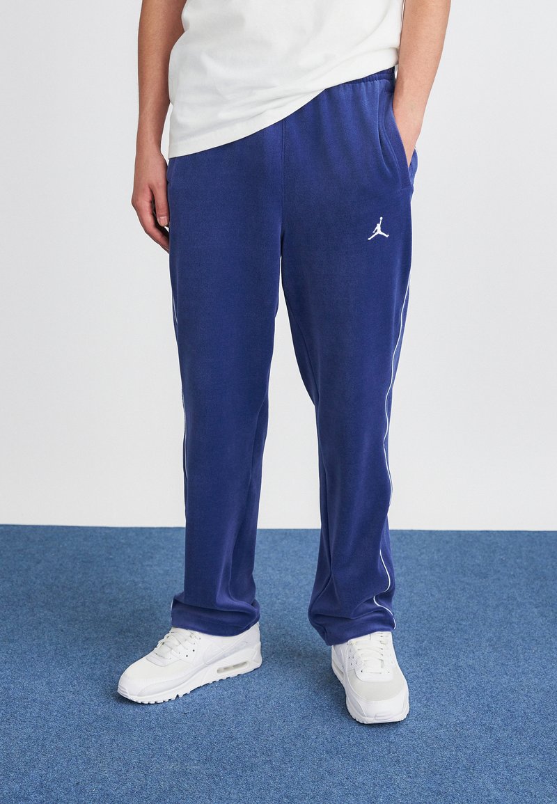 Tengerészkék melegítőnadrág fehér oldalsávokkal és Jumpman logóval, puha anyagból készült, rugalmas derékkal és oldalsó zsebekkel.