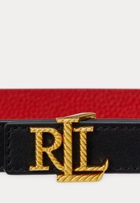 Črn usnjen pas z zlatim sponko v obliki vrvi, ki nosi inicialke "RL." Pas ima rdeč tekstilni poudarek.