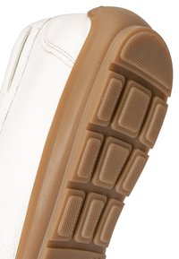 Chaussure blanche avec une semelle extérieure en caoutchouc brun texturée présentant des motifs rectangulaires antidérapants et des coutures blanches visibles sur la tige.