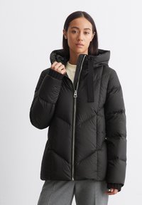 Giubbotto imbottito nero con zip frontale, cappuccio grande e polsini a coste, caratterizzato da un motivo geometrico a trapunta e una texture morbida.