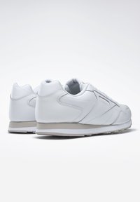 Weiße Leder-Sneaker mit glatter Textur, gepolstertem Kragen und geschichteten Designelementen. Hellfarbige Sohle mit Profilmustern.