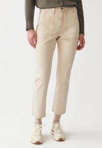 Beige high-waisted jeans with front pockets and contrasting stitching, paired with light-colored sneakers and ribbed beige socks.