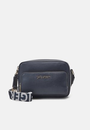 Marineblå rektangulær crossbody taske med lynlåslomme foran, guldlogo og aftagelig stofskulderrem med fed hvid tekst.