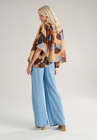Blusa dal taglio rilassato in un motivo multicolore di marroni e blu, abbinata a pantaloni a vita alta di un leggero blu con gamba larga e sandali con tacco blocco.