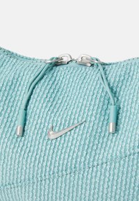 Light blue textured athletic top with a silver Nike logo and metallic zipper pulls. Features a rounded collar and a ribbed pattern.