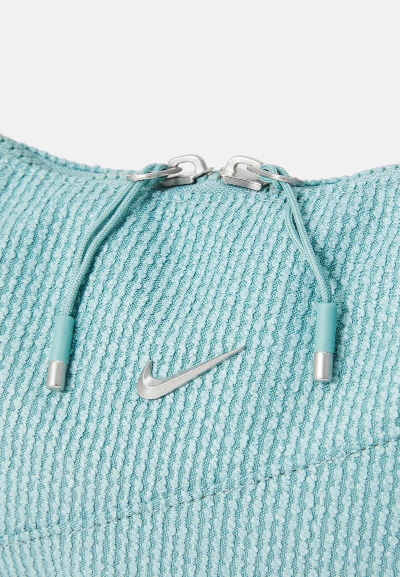 Top atletico azzurro con texture, logo Nike argentato e zip metalliche. Presenta un collo rotondo e un motivo a coste.