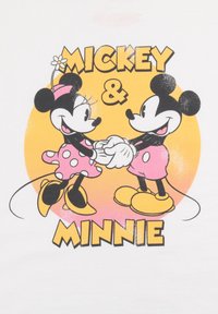 Camiseta gráfica con Mickey y Minnie Mouse. Los personajes son en blanco y negro sobre un fondo amarillo, con acentos rosas y lunares.