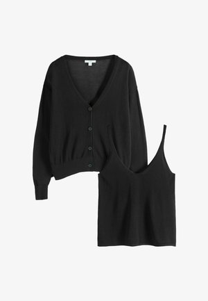 Fekete kötött kardigán gombokkal, és hozzáillő, ujjatlan, V-nyakú felső vékony pántokkal, mindkettő laposan fektetve fehér háttéren.