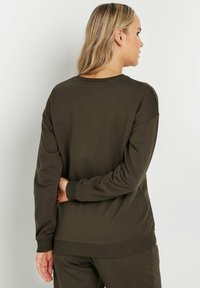 Sudadera verde oliva con cuello redondo, mangas largas y puños y dobladillo acanalados. Tejido suave, corte holgado y detalles mínimos en la parte posterior.
