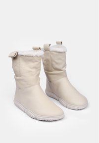 Botas de tobillo de cuero beige con forro de imitación de piel de oveja blanca, pestañas para tirar en los laterales y suelas de goma texturizadas para mayor agarre. Acabado exterior suave.