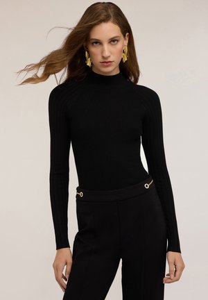Maglione a collo alto nero a coste con maniche lunghe, abbinato a pantaloni neri con un accento di catena in tono oro in vita.