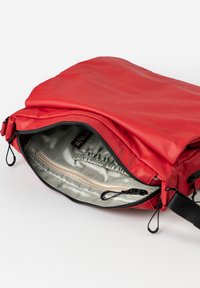 Borsa di stoffa rossa con chiusura a zip, caratterizzata da un esterno liscio e lucido e un interno di colore chiaro, liscio, con una piccola tasca a zip.