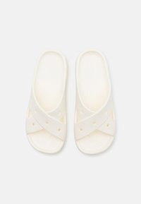 Sandales blanches à brides croisées fabriquées en matériau doux. Comprend des trous de ventilation et une semelle texturée pour le confort. Design plat, bout ouvert.