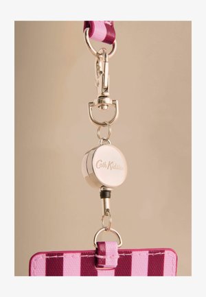Lanyard roz cu dungi, dotat cu un clips metalic și un suport retractabil rotund pe care este gravat "Cath Kidston", având o textură netedă.