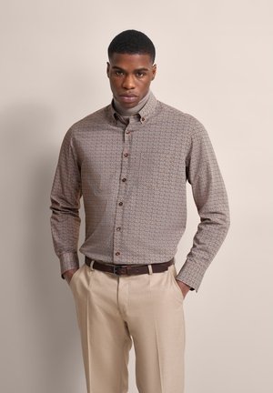 Button-up shirt featuring a brown and cream geometric pattern, long sleeves, and brown buttons, paired with light beige pants.