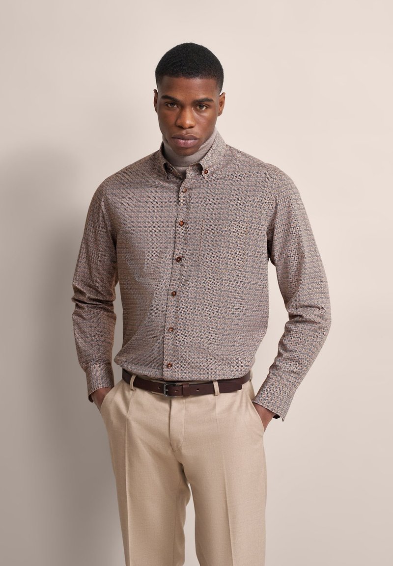 Button-up shirt featuring a brown and cream geometric pattern, long sleeves, and brown buttons, paired with light beige pants.