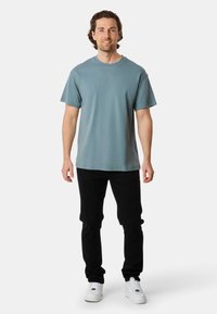 Ljusblå bomullströja med korta ärmar, rund halsringning, i kombination med svarta slim-fit byxor och vita sneakers. Avslappnad outfitpresentation.