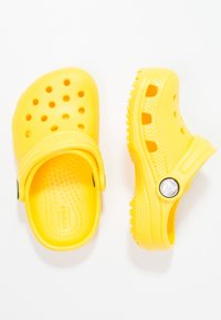 Sabots jaunes Crocs avec des trous de ventilation, un semelle texturée et une sangle arrière. Détail de logo rond sur le côté, construction en caoutchouc.