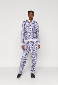 Survêtement à imprimé léopard aux tons violet et lilas, comprenant une veste zippée et un pantalon assorti avec poignets côtelés et coupe sportive.