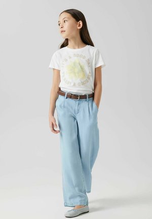 Camiseta blanca con el texto "Es un buen día" y un gráfico de flor amarilla, combinada con pantalones de pierna ancha azul claro y un cinturón marrón. Bailarinas grises.