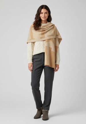 Châle beige à motifs drapé sur un pull crème en tricot torsadé, un pantalon gris à motifs et des bottines grises avec doublure en fourrure. Textures de tissu lisses.