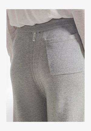 Grijze sweatpants van soepel stof, met een achterzak en een zichtbaar merketiket. De tailleband is ribbelig voor extra comfort.