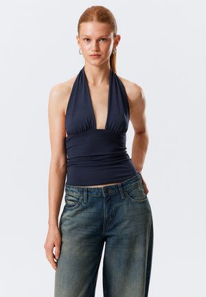 Top navy fără mâneci cu decolteu adânc în V, material adunat la bust și talie strânsă. Asortat cu blugi din denim albastru, cu croială lejeră.