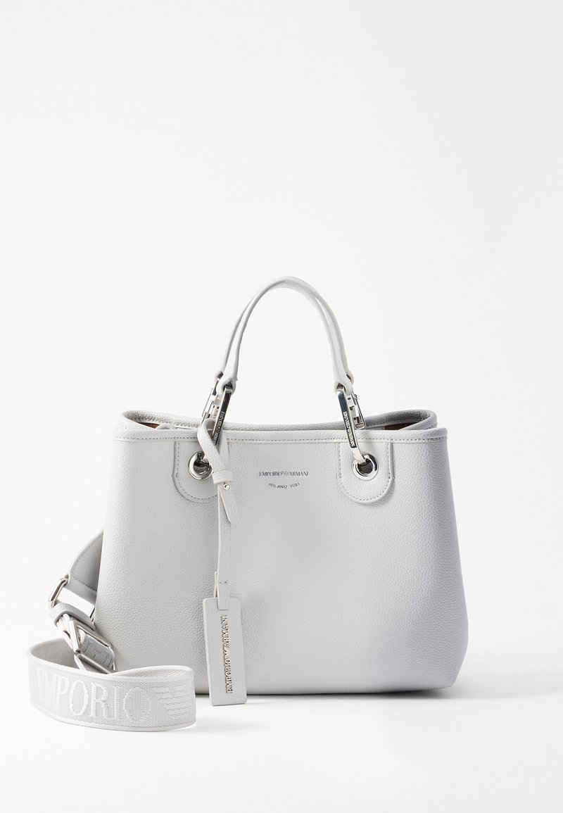 Fehér bőr kézitáska, két felső fogantyúval, ezüst színű kiegészítőkkel és levehető vállpánttal, amelyen logó található. Simább textúra és strukturált forma jellemzi.