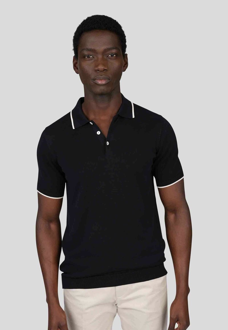Polo noir à manches courtes avec des accents blancs sur le col et les manches, présentant une patte à trois boutons et une coupe ajustée.