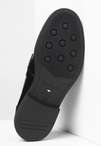 Semelle de chaussure en cuir noir avec des motifs circulaires et un logo de marque en relief. Présente une texture lisse et inclut des informations sur la taille.