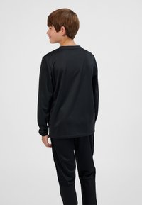 Top deportivo negro de manga larga con cuello redondo, textura suave y ajuste slim, combinado con pantalones negros a juego. Vista desde atrás, diseño minimalista.