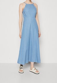 Vaaleansininen farkkukangas maxi-mekko, jossa on ohuet olkaimet, vartalonmyötäinen yläosa ja levenevät helmat. Yhdistetty valkoisiin sandaaleihin, joissa on koristeneula.