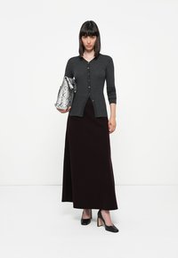 Grå ribbete cardigan med knapper foran, brukt over et langt bordeaux skjørt. Akkompagnert av en sølvfarget clutch i slangeskinn og svarte blokkhelsesko.