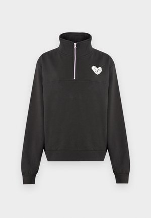 Fekete, negyedrészes cipzáros polár felső magas gallérral, bordázott mandzsettákkal és szegéllyel, a mellkason egy kis, fehér szív alakú grafikával.