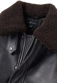 Giacca di pelle nera con colletto in shearling marrone. Presenta cerniere metalliche, bottoni a pressione e dettagli a coste sui lati.