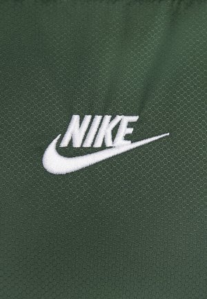 Groene textuurstof met een witte geborduurde Nike-logo met een swoosh, tegen een hexagonaal patroon.