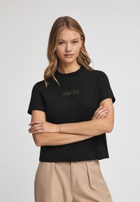 Camiseta negra corta con mangas cortas, que presenta un logotipo bordado en tono "Polo Club" en el pecho. Tejido de algodón suave.