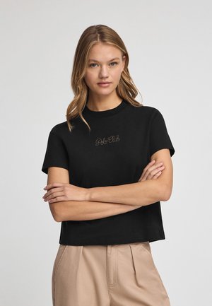Camiseta negra corta con mangas cortas, que presenta un logotipo bordado en tono "Polo Club" en el pecho. Tejido de algodón suave.