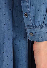 Denimskjorta i ljusblå färg med små marinblå prickar. Knäppt ärm med matchande knapppdtalj. Mjuk textur.