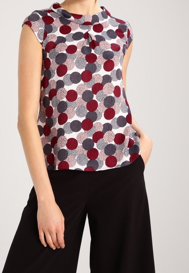 Blusa de manga corta con cuello redondo, que presenta un estampado de lunares en rojo, azul marino y crema sobre un fondo claro. Tejido suave, corte holgado.