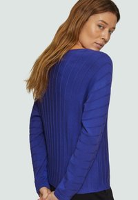 Blaues geripptes Sweatshirt mit langen Ärmeln, das über eine vertikale Streifenstruktur und eine lockere Passform verfügt. Der Stoff wirkt weich und leicht.