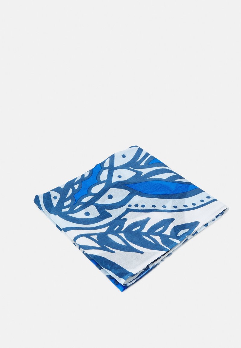 Tissu plié avec un motif abstrait bleu et blanc de feuilles et de points, posé sur un fond blanc uni.