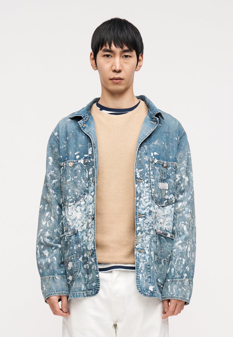 Μπλε τζιν μπουφάν με ξεθωριασμένο  μπλε χρώμα και σχέδιο με πιτσιλιές μπογιάς. Διαθέτει διπλές τσέπες στο στήθος, μεταλλικά κουμπιά και άνετη εφαρμογή.