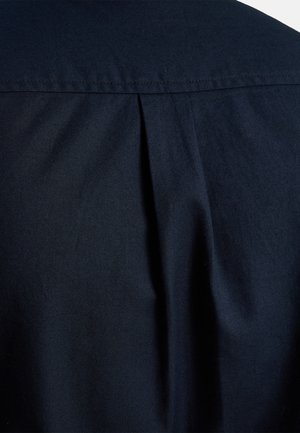 Granatowy materiał koszuli pokazujący widok z tyłu z subtelnym detalem w postaci zakładki. Tekstura wydaje się gładka i lekko tkana, z wyraźnym kołnierzykiem.