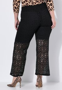 Zwarte kant broek met een bloemenpatroon en een semi-transparant ontwerp. De tailleband is glad en ze hebben een wijde pijp.