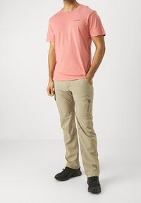 Ljusrosa bomullströja med rund hals och korta ärmar, tillsammans med beige cargobyxor med flera fickor, stående på svarta skor.